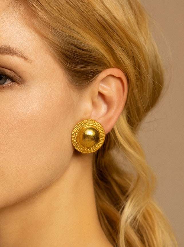 A model wearing Lalounis 18 Karat Yellow Gold Circle Dome Stud Earrings - V50619 by Vivid Diamonds, highlighting the earrings' exquisite craftsmanship and bold elegance against a chic hairstyle.