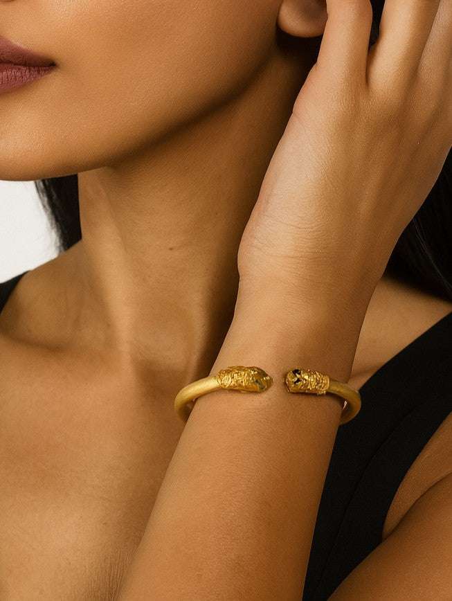 Model wearing the 18K Yellow Gold Double Lion Cuff Bracelet with Ruby Eyes & Emerald Accents by Vivid Diamonds, showcasing its luxurious design and elegant style.